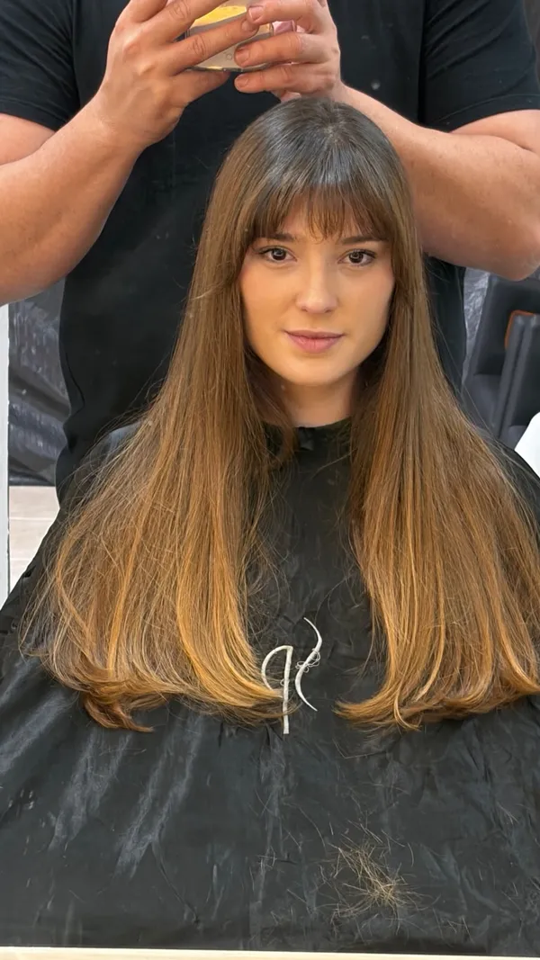 Mulher com cabelo longo liso, franja e pontas em tom caramelo, sentada na cadeira do salão