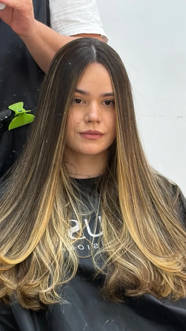 Mulher com cabelo longo liso, raiz escura e pontas em tom de loiro dourado