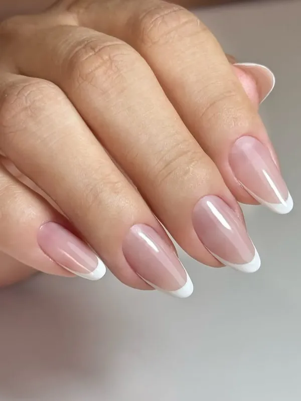 Mão com unhas amendoadas em francesinha branca clássica sobre base rosada