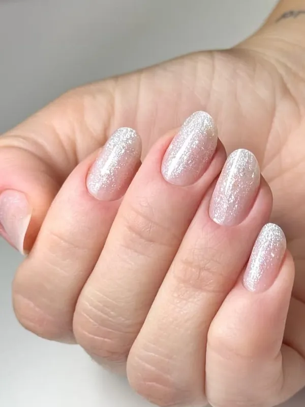 Mão com unhas curtas ovais em base rosada com brilho prateado