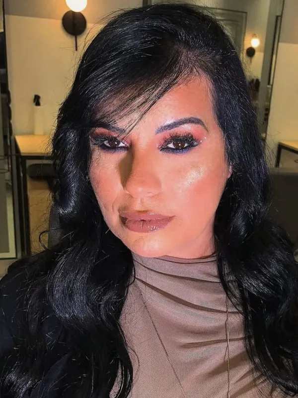 Mulher com cabelo preto ondulado e maquiagem com sombra rosada e azul e brilho no olhar