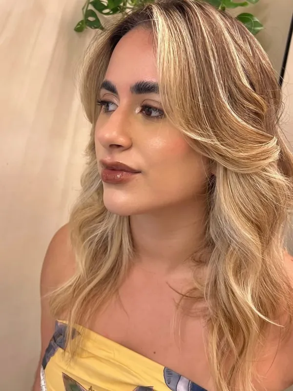 Mulher de perfil com cabelo loiro em camadas com franja lateral e sobrancelhas marcadas