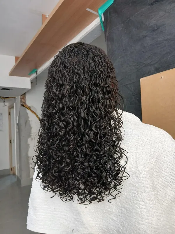 Mulher de costas com cabelo escuro com cachos definidos, longo e molhado, sobre toalha branca