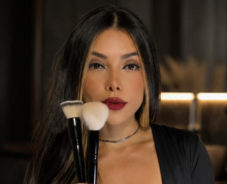 Dayana Fitzner, maquiadora, segurando dois pincéis de maquiagem diante do rosto.