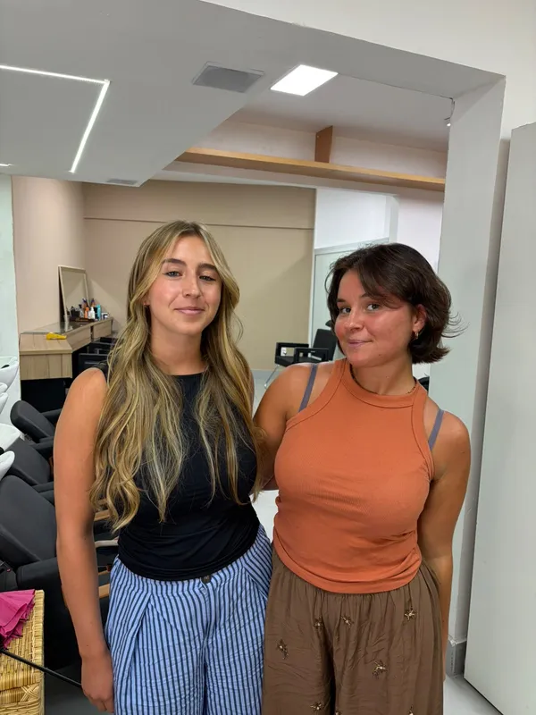 Duas clientes sorrindo lado a lado, uma com cabelo longo loiro e outra com corte curto castanho