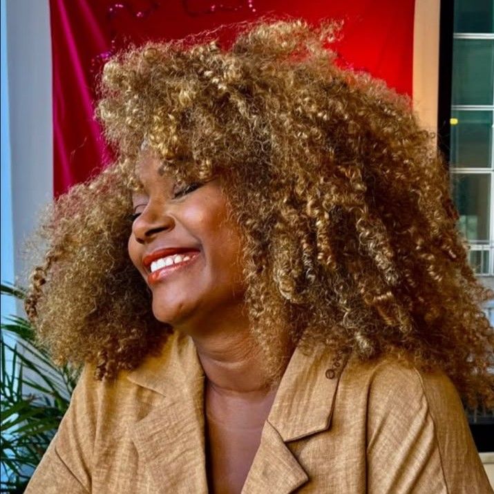 Ju Gomes sorrindo, com cabelo cacheado volumoso e blazer bege.